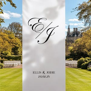 Puede incluir: Una pancarta blanca con iniciales y texto caligráficos negros, colgada en un jardín. La pancarta dice "ELLIS & JODIE" y "24.02.25". El fondo presenta un césped cuidado, árboles y un castillo.