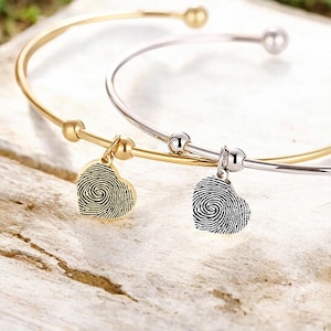 May include: Two gold and silver bangle bracelets with heart-shaped charms. The charms have a fingerprint design.