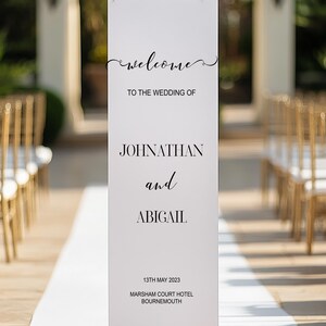 May include: A white wedding sign with black text. The sign says "welcome", "TO THE WEDDING OF", "JOHNATHAN and ABIGAIL", "13TH MAY 2023", and "MARSHAM COURT HOTEL BOURNEMOUTH". The sign is displayed at a wedding ceremony.