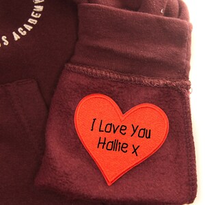 Op de afbeelding: Een maroon hoodie met een rode hartvormige patch waarop "I Love You Hollie X" staat.