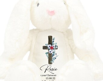 May include: White plush bunny with a cross and floral design on its chest. The bunny has the name "Rosie" and the text "1 your Christening 13.08.22 St Peter's Chu" printed on its chest.