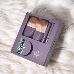 May include: Purple makeup brush set with a floral design and the name "Debbie" on the front.