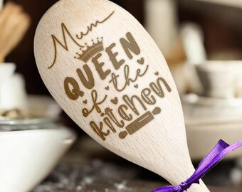 May include: Wooden spoon with the text "Mum Queen of the Kitchen" engraved on it. The spoon is light brown and has a purple ribbon tied around the handle.