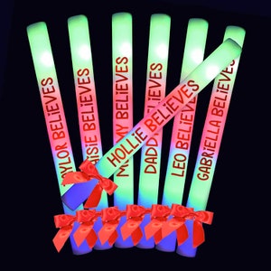 May include: Seven glow sticks with red text on a black background. The text on the glow sticks reads "Taylor Believes", "Maisie Believes", "Hollie Believes", "Daddy Believes", "Leo Believes", "Gabriella Believes". Each glow stick has a red bow tied around it.