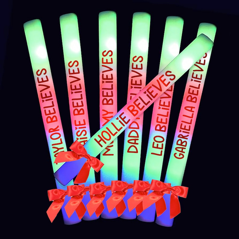 May include: Seven glow sticks with red text on a black background. The text on the glow sticks reads "Taylor Believes", "Maisie Believes", "Hollie Believes", "Daddy Believes", "Leo Believes", "Gabriella Believes". Each glow stick has a red bow tied around it.