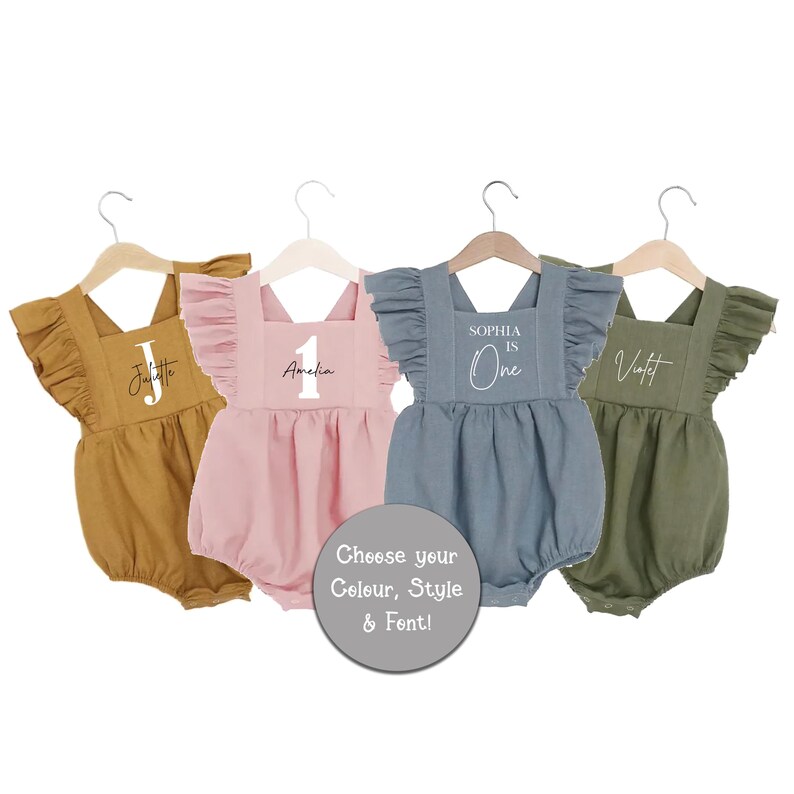 May include: Four personalized baby onesies in different colors. The onesies have ruffles on the shoulders and say "Juliette", "Amelia 1", "Sophia is One", and "Violet".