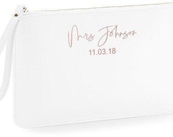 May include: White zippered clutch bag with a gold zipper and a wrist strap. The bag has the text "Mrs Johnson" and the date "11.03.18" printed in rose gold.