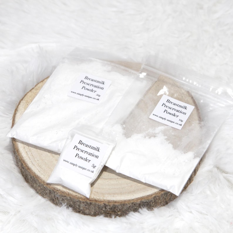 May include: Three clear plastic bags filled with white powder labeled "Breastmilk Preservation Powder" on a wooden slice. The bags contain 5g, 10g, and 50g of powder. The background is a soft, white, textured surface.