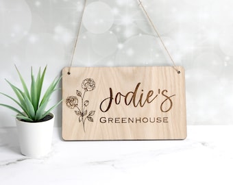 Könnte beinhalten: Ein Holzschild mit einem floralen Design und dem Text "Jodie's Greenhouse" eingraviert.