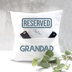 May include: White pillow with a pocket for a remote control. The pillow has the text "RESERVED for GRANDAD" printed on it in blue.