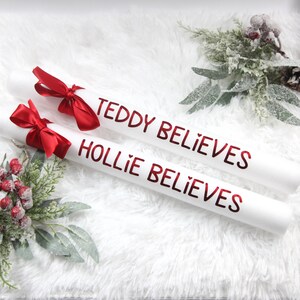 May include: Two white gift wrapping tubes with red bows and the text "Teddy Believes" and "Hollie Believes" in red lettering.