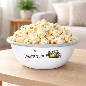 Pode incluir: Uma tigela de pipoca esmaltada branca cheia de pipoca estourada. A tigela tem uma borda cinza e apresenta o texto "The Watson's" e um gráfico "Movie Night!"