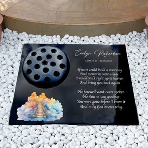 Puede incluir: Placa conmemorativa de granito negro con un portaflor, una imagen de acuarela de una escalera al cielo y el texto "Evelyn Richardson 13.05.1949 - 28.08.2023" y un poema sobre recuerdos y despedidas.