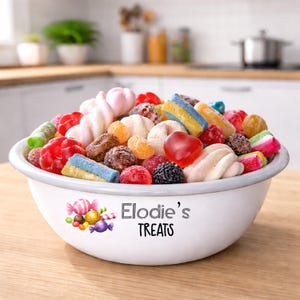 Pode incluir: Uma tigela de esmalte branco cheia de uma variedade colorida de doces, incluindo ursinhos de goma, marshmallows e doces duros. A tigela é decorada com um gráfico de doces e o texto "Elodie's TREATS".