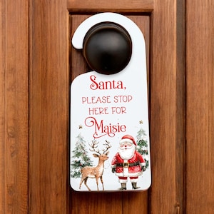Op de afbeelding: Witte deurhanger met een afbeelding van de kerstman en een rendier. De tekst luidt "Santa, Please Stop Here For Maisie".