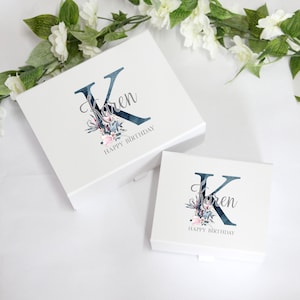 May include: Two white gift boxes with blue and pink floral designs. The larger box has the letter "K" and the name "Karen" with the text "Happy Birthday". The smaller box has the same design but is smaller.