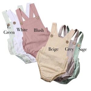 May include: Five baby onesies in different colors: green, white, blush, beige, grey, and sage. Each onesie has a button closure and adjustable straps.