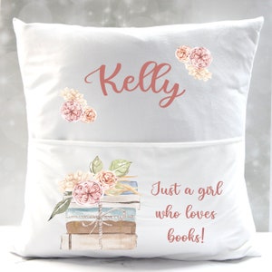 May include: White pillow with a pocket on the front. The pillow has a floral design and the text "Kelly" and "Just a girl who loves books!" printed on it.