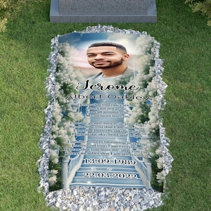 May include: A blue and white memorial headstone with a photo of a young man. The headstone has the name "Jerome Albert Oakley" and the dates "13.09.1989" and "22.03.2022". The headstone also has a poem about the deceased.