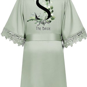May include: Sage green satin robe with a lace trim. The robe features a floral design with the letter "S" and the text "Sasha The Bride".