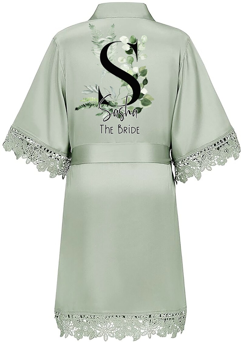May include: Sage green satin robe with a lace trim. The robe features a floral design with the letter "S" and the text "Sasha The Bride".