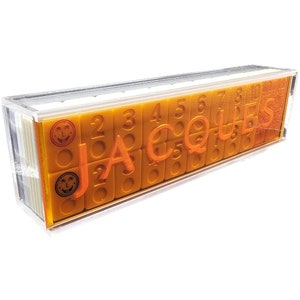 May include: A clear plastic case filled with orange dominoes. The dominoes have black dots and the word "JACQUES" is printed on the case.