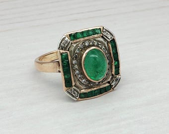 May include: A gold ring with a large oval emerald centre stone. The ring is surrounded by smaller emeralds and diamonds, set in a square design. The ring's band is gold.