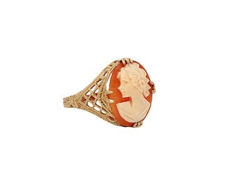 May include: A gold-toned ring featuring an oval cameo with a profile of a woman. The cameo is set in an orange-red background. The ring has a filigree design on the band and around the cameo.