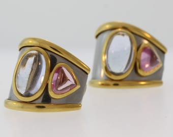 May include: A pair of gold and silver tone earrings with clear and pink gemstones. The earrings are shaped like a curved band with three gemstones set in the center.