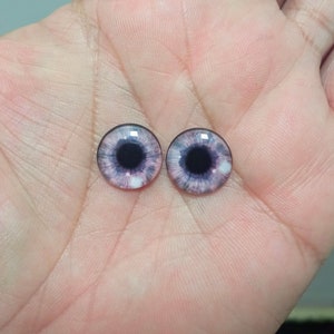 May include: Two round glass doll eyes with a pink and purple iris and a black pupil.