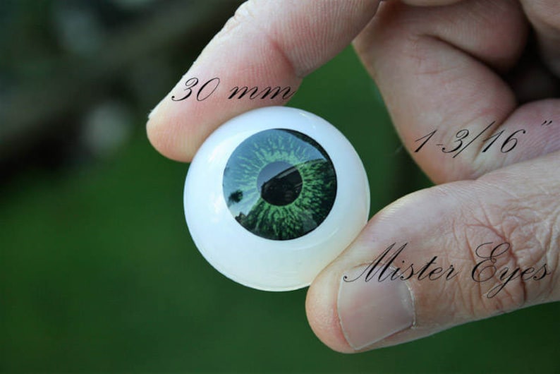 May include: A close-up of a 30 mm (1-3/16") green glass eye, with a white sclera, held in a hand. The text "Mister Eyes" is visible in the image.