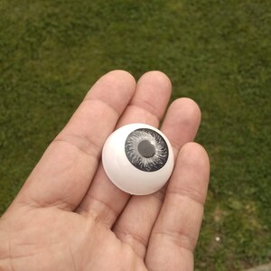 May include: A white plastic doll eye with a black and grey iris.