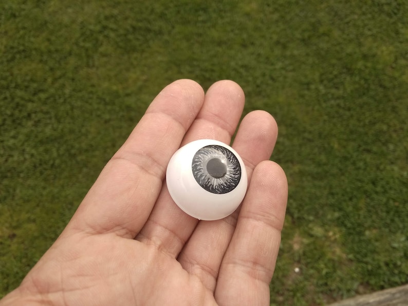 May include: A white plastic doll eye with a black and grey iris.