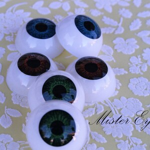 May include: Five different coloured doll eyes, with white plastic surrounds. The eyes are blue, brown, green, and two shades of green. The text "Mister Eyes" is visible in the bottom right corner of the image.