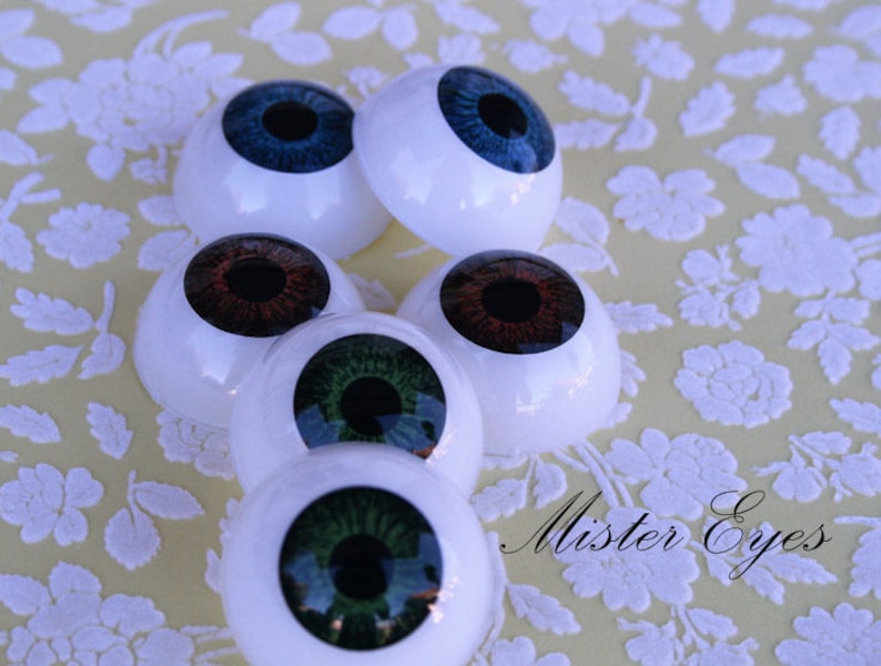 May include: Five different coloured doll eyes, with white plastic surrounds. The eyes are blue, brown, green, and two shades of green. The text "Mister Eyes" is visible in the bottom right corner of the image.