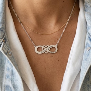 May include: A layered necklace set featuring a thin gold chain and a silver-toned infinity symbol pendant integrated with a heart shape. The silver pendant is engraved with the text "Jessie & Jerome" and the date "06-07-23" on the infinity loops.
