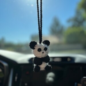 May include: A black and white crocheted panda bear hanging from a rearview mirror in a car.