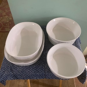 May include: Set of four white ceramic baking dishes of varying sizes. The dishes are all round and have a smooth, white finish.
