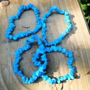 May include: Three turquoise blue gemstone chip bracelets on a wooden surface.