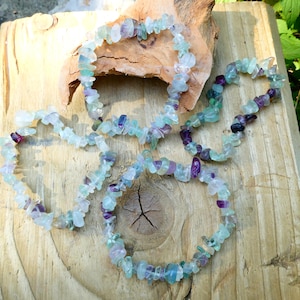 May include: Four bracelets made of green, blue and purple fluorite chips. The bracelets are arranged on a wooden surface.