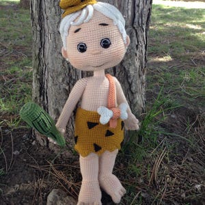 May include: A crocheted doll of a cartoon character with a white hat, brown and black clothing, and a green stick in its hand.