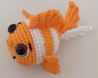May include: A handmade crochet fish in orange and white, featuring large black eyes and detailed fins. The fish has a cheerful expression and is designed with a striped pattern on its body. A whimsical, soft toy.