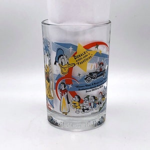 May include: A clear glass tumbler featuring colorful Disney character graphics, including Donald Duck, Snow White, and the Seven Dwarfs. Text on the glass reads: DONALD'S middle name is "Fauntleroy." and "Disney Stars & Motor Cars" Parade features classic American cars from 1929 to 1951.