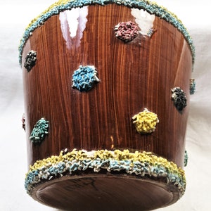 Puede incluir: Un recipiente de cer&aacute;mica marr&oacute;n con un acabado brillante, decorado con acentos texturizados coloridos. El borde y las manchas dispersas presentan chispas azules, amarillas, rojas y negras. El recipiente tiene un aspecto de vetas de madera.