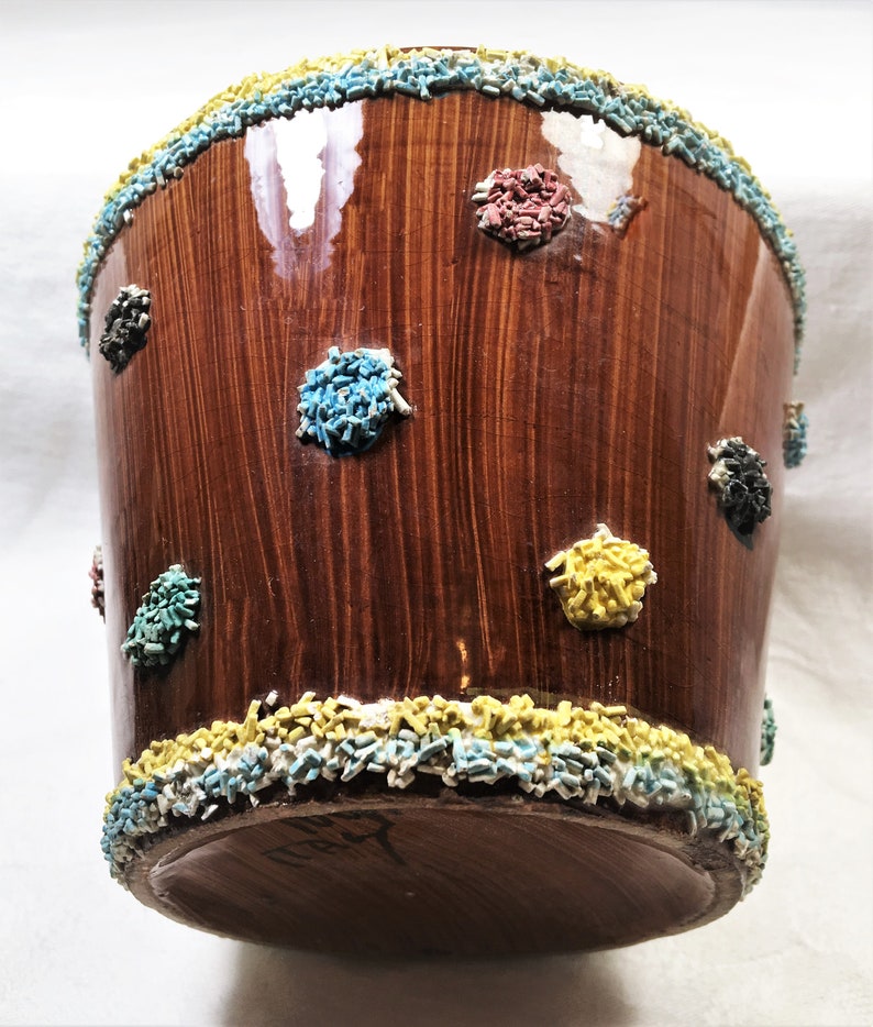 Puede incluir: Un recipiente de cer&aacute;mica marr&oacute;n con un acabado brillante, decorado con acentos texturizados coloridos. El borde y las manchas dispersas presentan chispas azules, amarillas, rojas y negras. El recipiente tiene un aspecto de vetas de madera.