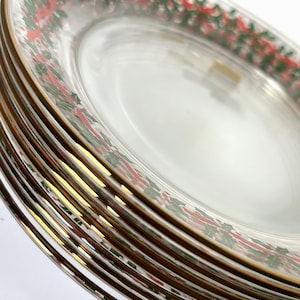May include: A stack of clear glass plates with a gold rim and a festive red and green floral design around the edge. The plates are stacked on top of each other, showcasing the design.