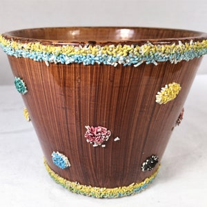 May include: A brown ceramic planter with a textured surface and decorative sprinkles. The planter has a wide top and tapers down. Colorful sprinkles adorn the rim and are scattered across the exterior in various colors, including yellow, blue, and pink.