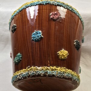 Puede incluir: Un recipiente de cer&aacute;mica marr&oacute;n con acabado brillante, decorado con confeti de colores alrededor de los bordes superior e inferior, y dispersos por la superficie. El confeti es en tonos azul, amarillo, rojo y negro. El recipiente tiene forma cil&iacute;ndrica.