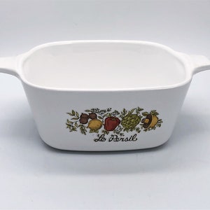 May include: White rectangular casserole dish with handles, decorated with a colorful fruit and vegetable design. The words "Le Persil" are printed below the design. A vintage kitchenware item.