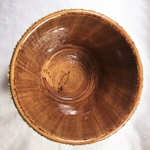 Puede incluir: Un cuenco de madera hecho a mano con un acabado marr&oacute;n c&aacute;lido natural. El interior muestra un patr&oacute;n de vetas en espiral, y el borde est&aacute; adornado con un ribete dorado decorativo. El dise&ntilde;o del cuenco sugiere que podr&iacute;a usarse para servir o exhibir.